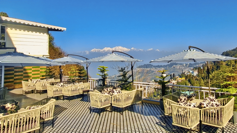 Wide shot of a sunny outdoor restaurant deck overlooking lush hills and snow-capped peaks | Voyage Rodhi Resort