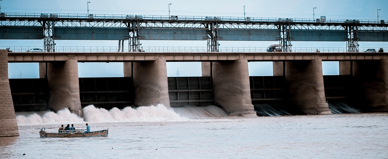 Large dam releasing water with people boating near the base.