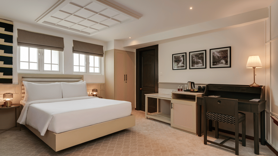 Deluxe Room at Shilton Suites, Bengaluru, featuring a king size bed, bedside tables, work desk, upholstered seating area and large windows.