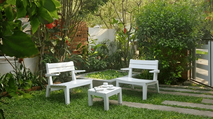 White garden seating set on a green lawn surrounded by trees and plants at Amanvana Spa Resort in Coorg.