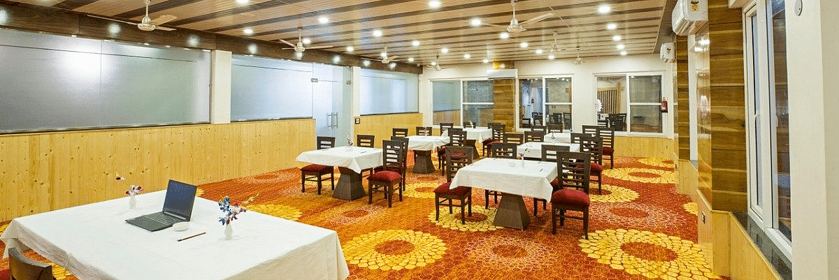 A warmly lit Banquet Hall with a fully carpeted floor along with tables set with white table cloth at Regenta Inn DLS.