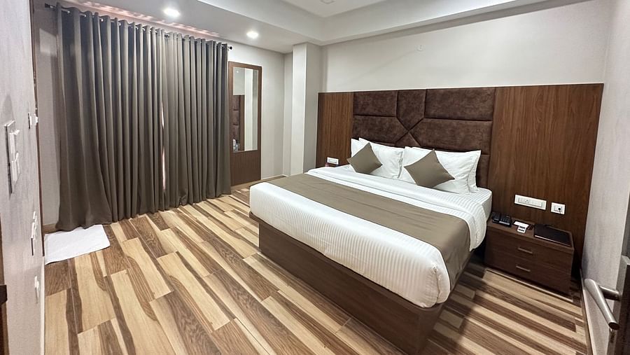 A bedroom with two single beds, dark wooden headboards, a ceiling fan, and light wooden flooring is pictured - Kankidham Lords Inn