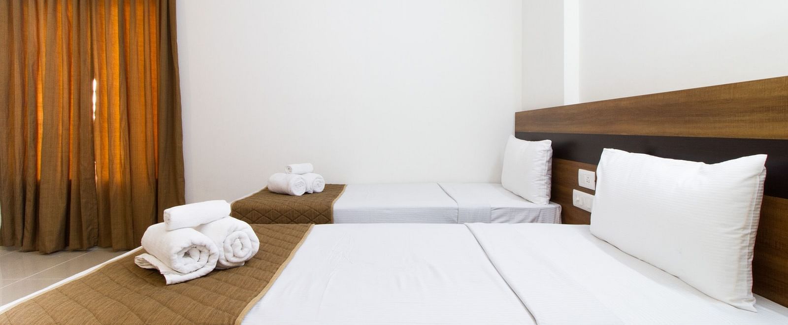 A room featuring twin beds with brown accents and neatly rolled white towels at Sanctum Suites Whitefield, Bangalore.