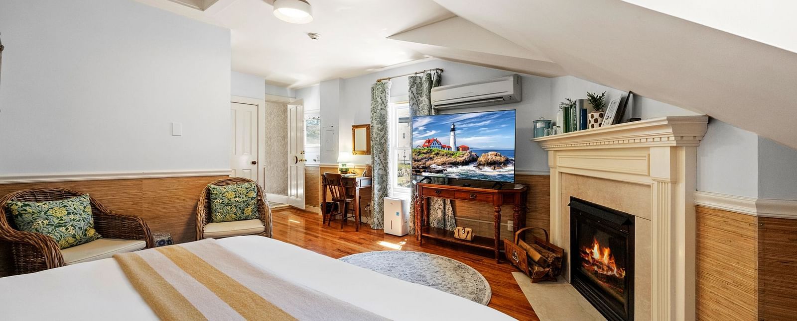 A room with king size bed, fireplace, a pair of chairs placed near the bed and a tv at Hartstone Inn.