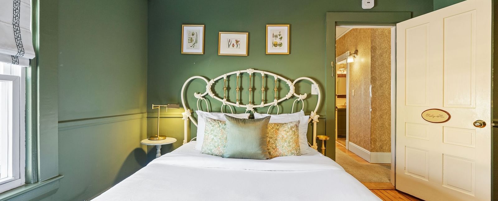 Green-walled bedroom with white iron bed with framed arts in the wall at Hartstone Inn.