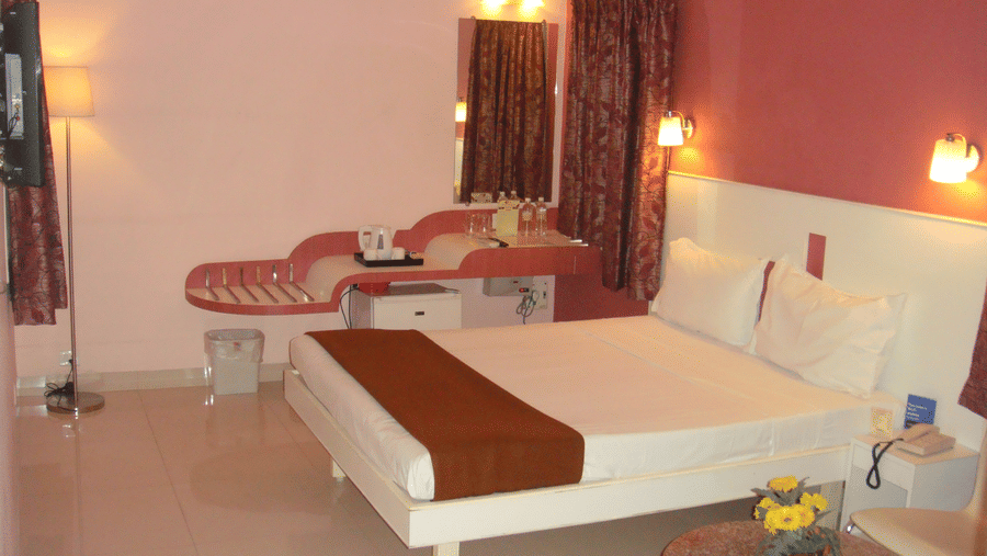 A well-appointed hotel bedroom with a double bed, soft pink and dark maroon walls, and a dedicated vanity mirror desk - Hotel Pandian