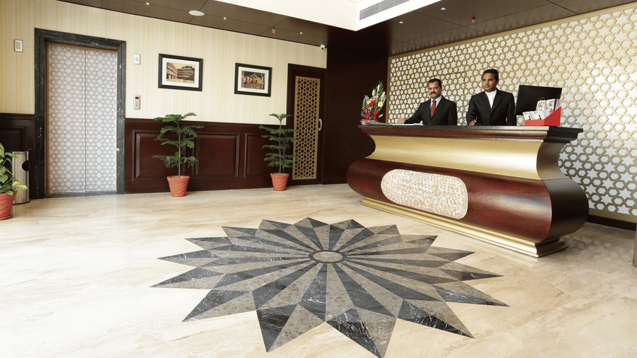 A reception area at Comfort Inn Sapphire by Eastlynn Collections, Jaipur with front desk, staff, lift, potted plants, and patterned floor design.