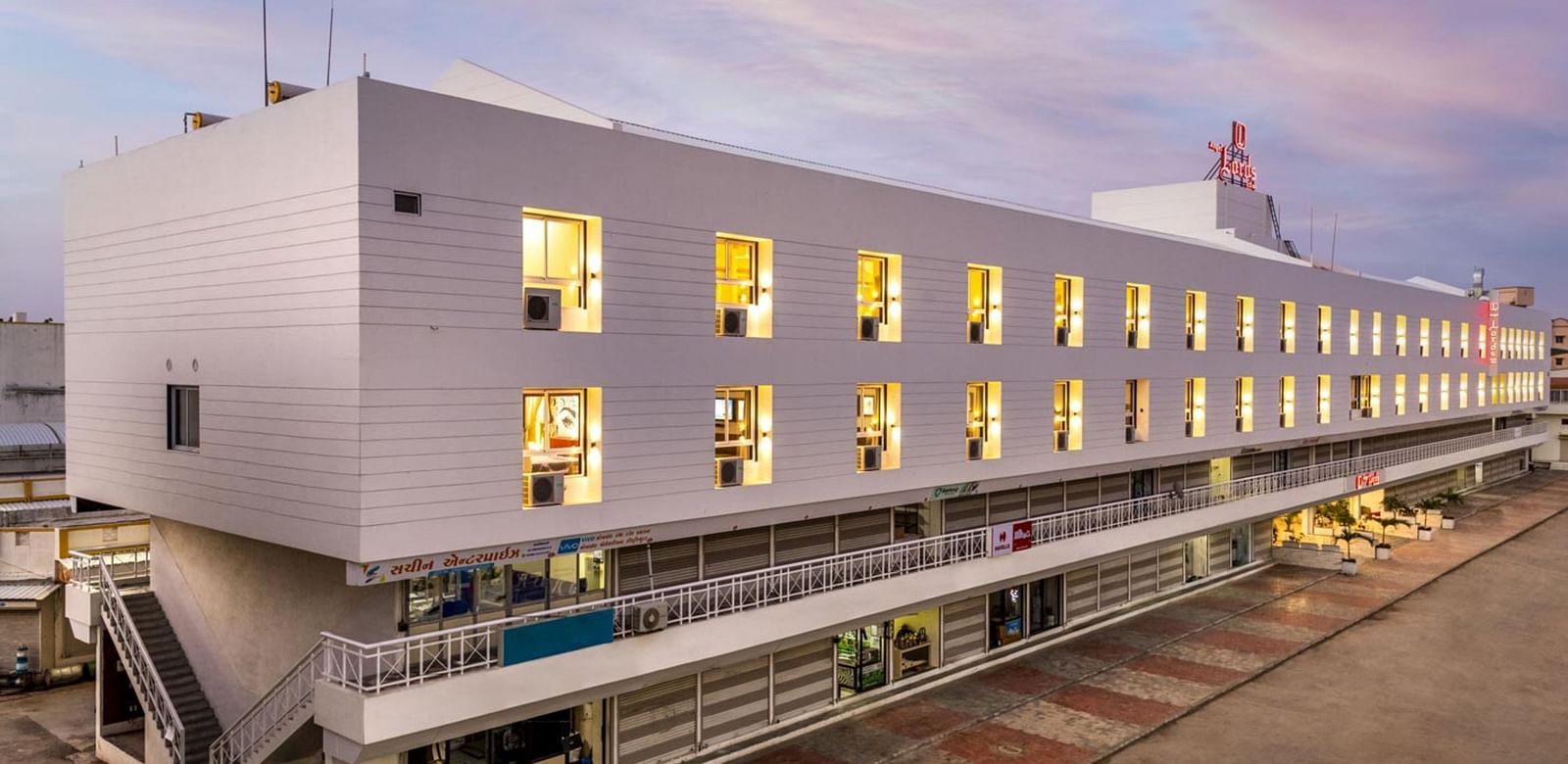 An exterior view at Angel Lords Eco Inn Amreli with many illuminated windows at dusk.