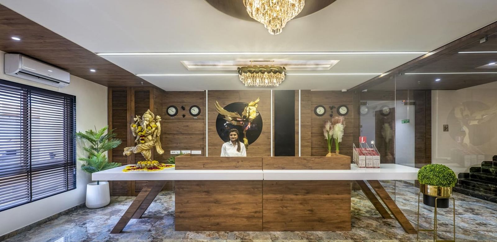 A well-lit hotel reception area with a wooden front desk and seating area towards the side at Angel Lords Eco Inn Amreli.