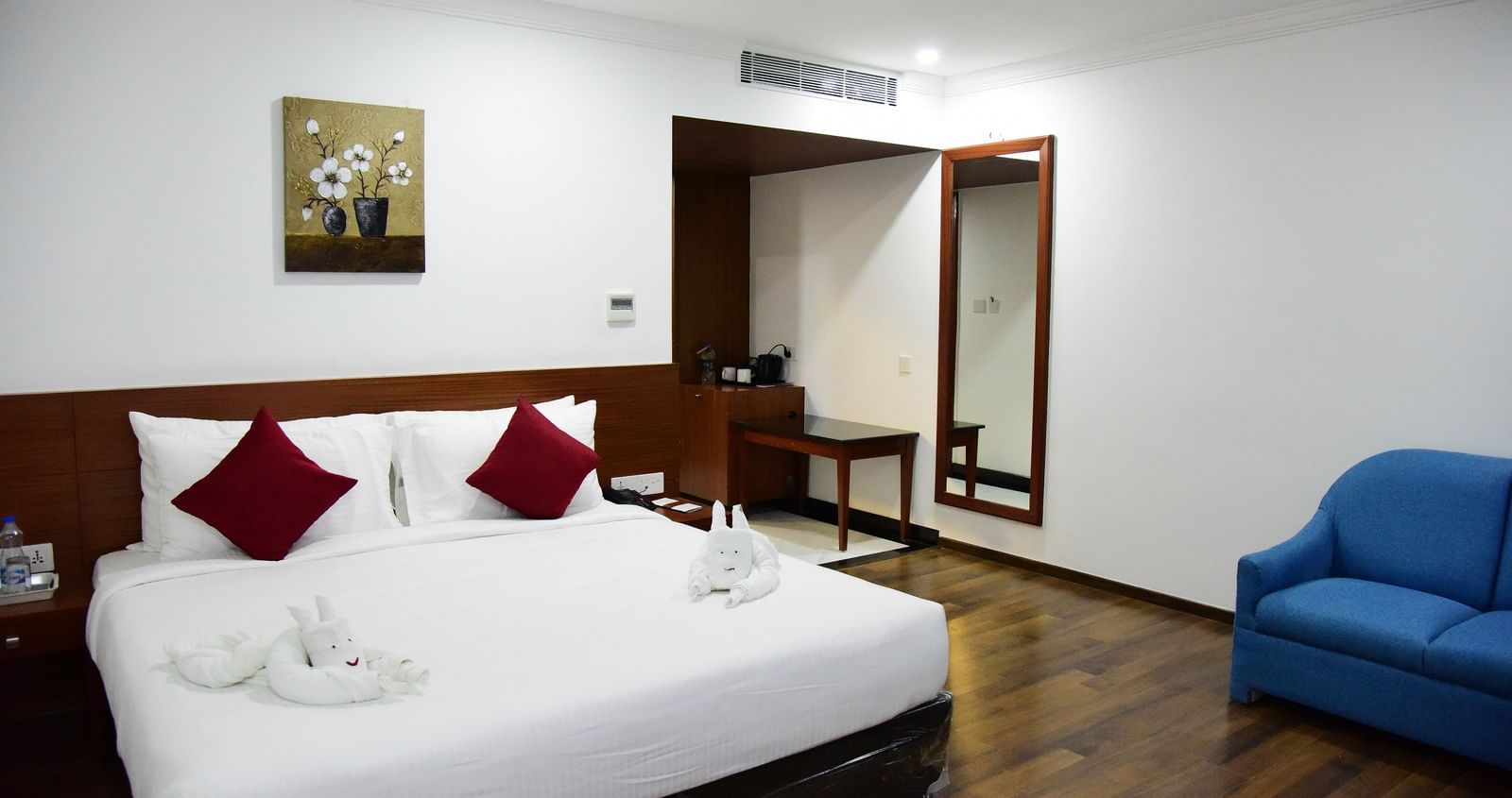 A bright and modern studio room at The Royal Comfort, featuring a comfortable bed with white linens and a stylish teal runner, along with a sleek workspace.
