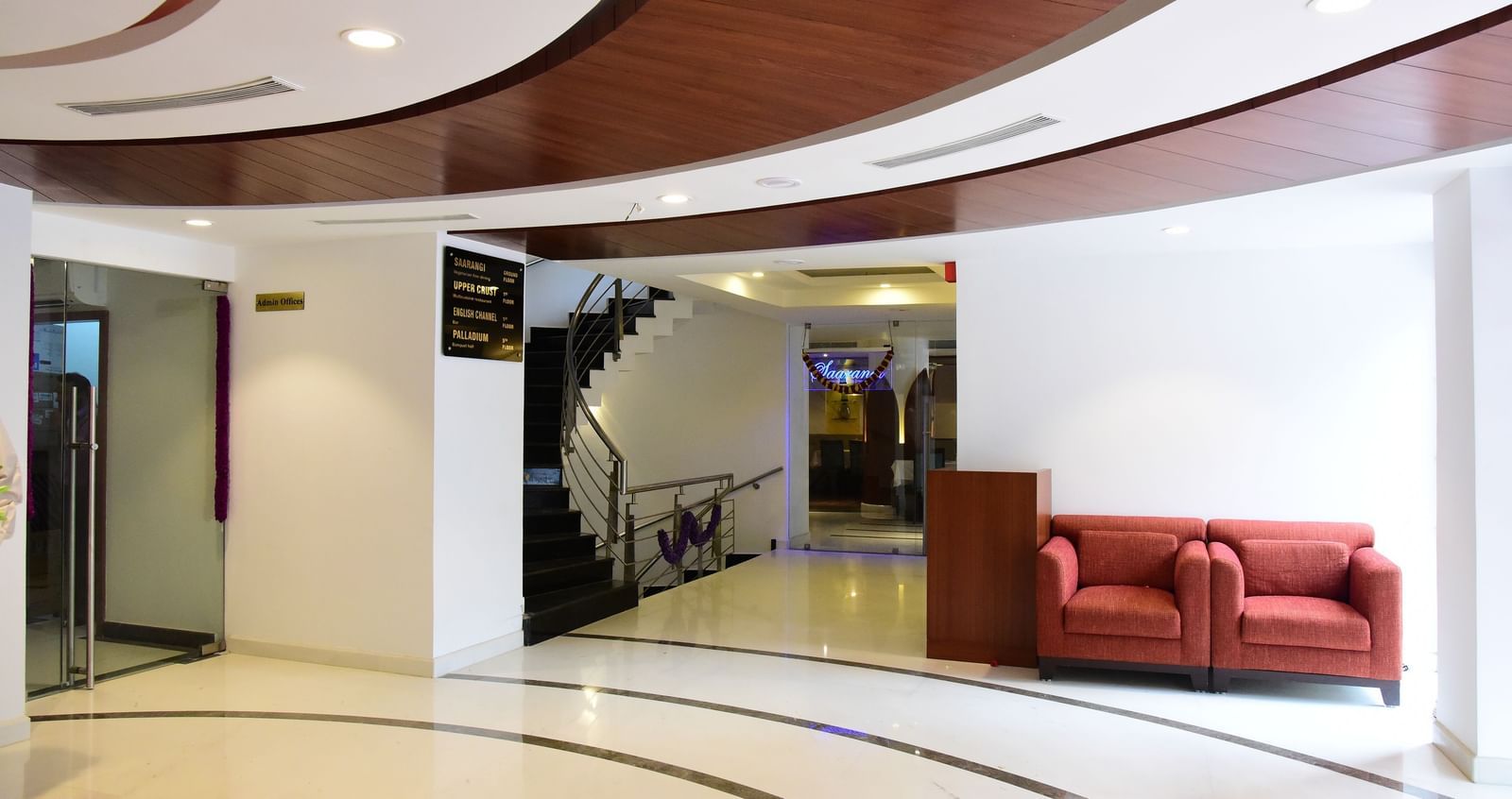The contemporary and spacious lobby of The Royal Comfort, showcasing a curved ceiling design and a small seating area with red sofas.