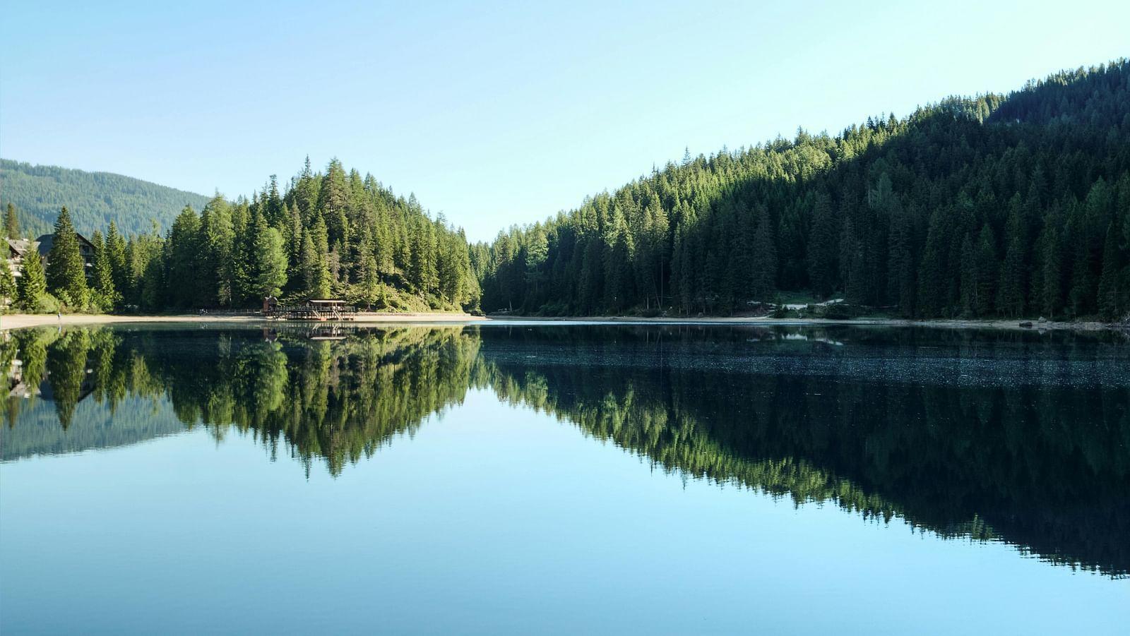Serene lake reflecting the surrounding forest and clear blue sky.