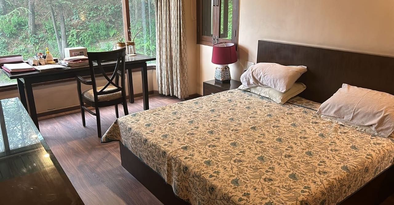 A large bed near a nightstand with a view of trees at Presidential Suite at SOUTHGATE KASAULI BY ZENQ.