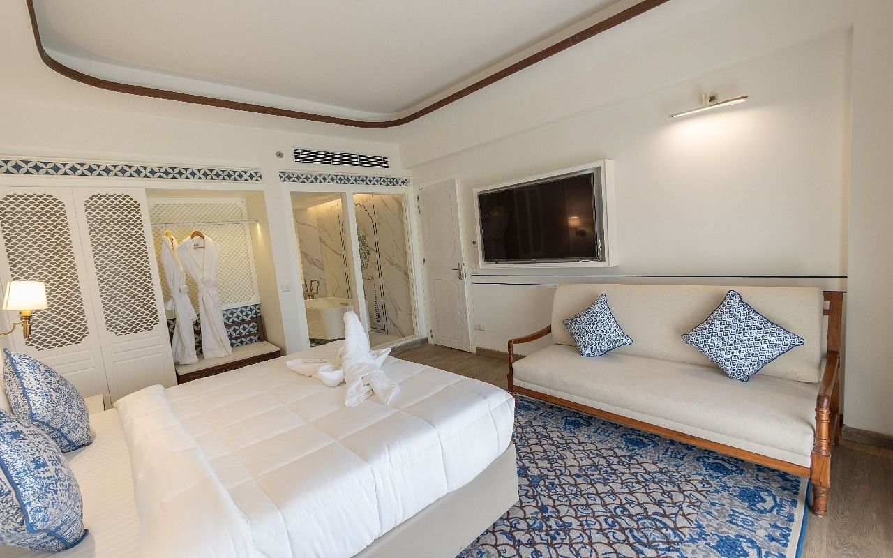 Corner view shot of the bedroom at Ananata Room featuring a plush double bed alon with a television and a couch in front of it at Bhagirathi by RDB Atishay.