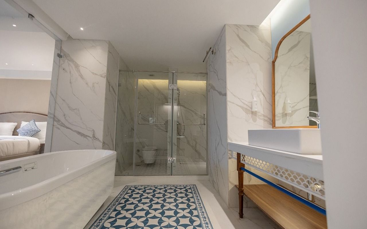 A brightly lit bathroom featuring a bathtub and a well stocked vanity area of the Purna Room at Bhagirathi by RDB Atishay.