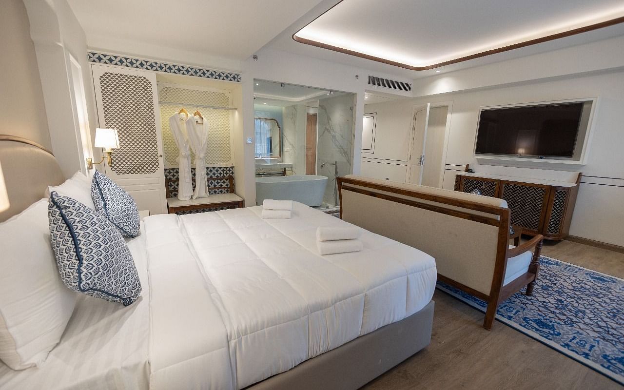 Corner view shot of the Purna room featuring a soft double bed with neatly arranged cushions along with a wall mounted television at Bhagirathi by RDB Atishay.