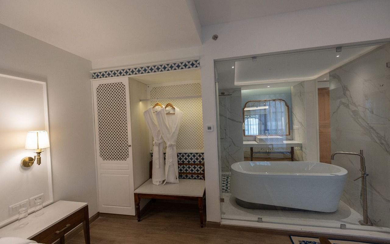 A bathtub in the bathroom of the Purna Room separated by a glass partition alongside a wardrobe at Bhagirathi by RDB Atishay. 