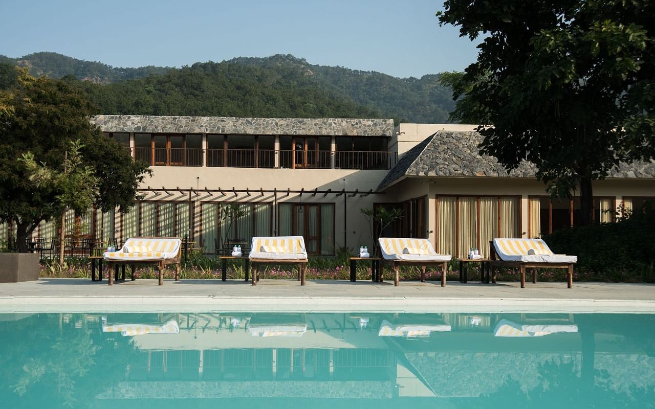 The outdoor swimming pool at Saraca Resort & Spa Corbett with lounging chairs placed in the backdrop