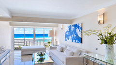 A stylish beachfront living room at The Soco Hotel, Barbados featuring modern furnishings, wall art, expansive windows, and a stunning ocean view.