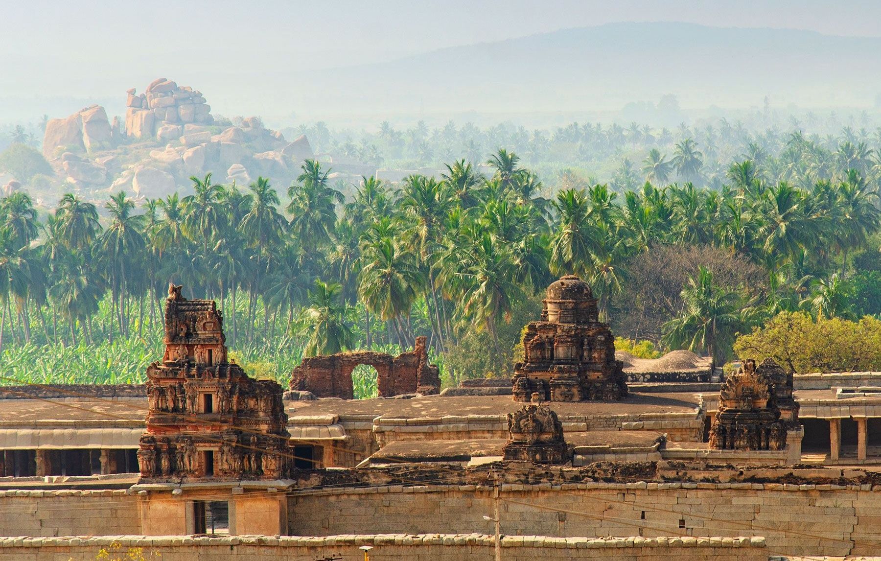 Ancient temple ruins and coconut trees in Hampi, India.