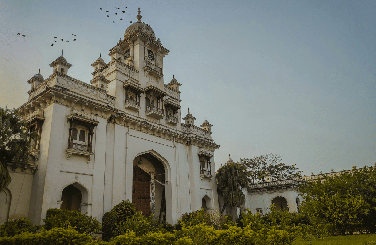 A white stone building with an arched entrance and ornate carvings under a sky with birds