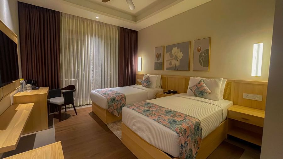 A twin room with separate bedding for two people, each having cushions and coverlets with similar print. A study desk and chair, a television and wall paintings are also visible.
