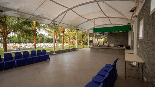 A large, empty indoor event space with a high arched ceiling, ready for setup, with rows of blue chairs stacked against a wall - Grande Bay Resort & Spa, Mamallapuram