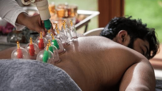 Man receiving cupping therapy on back, colorful cups, blurred background, close-up shot of treatment- Shreyas Retreat