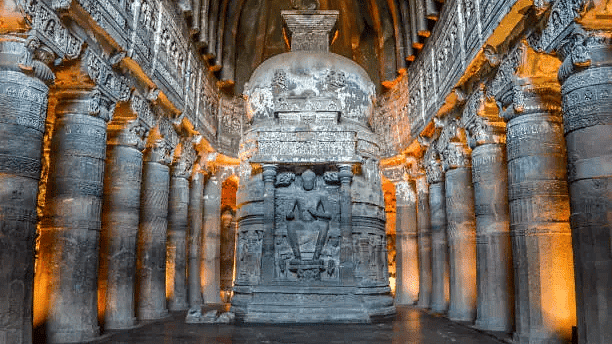 Interior view of ancient rock-cut cave with sculpted pillars and detailed carvings.