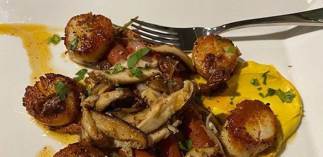 A plate of pan-seared scallops with a mushroom and potato hash, drizzled with a balsamic glaze.