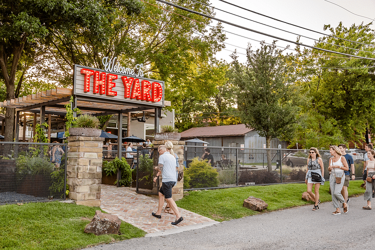 Man walking into a place with a board titled the yard while a group of women walk through a paved road.
