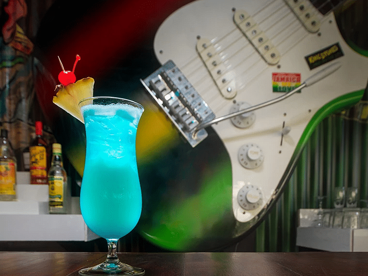 A blue cocktail placed on a counter with a wall mounted guitar in the background - S Hotel Kingston, Jamaica