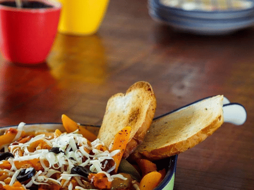 a plate of pasta placed on a wooden table featuring potted plants in the backdrop