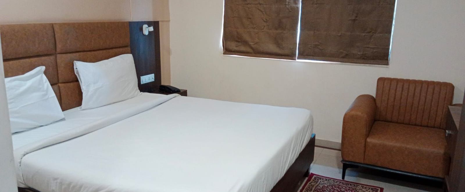 Side view of a double bed at Pravasa Ahmedabad with a brown leather armchair in the corner.