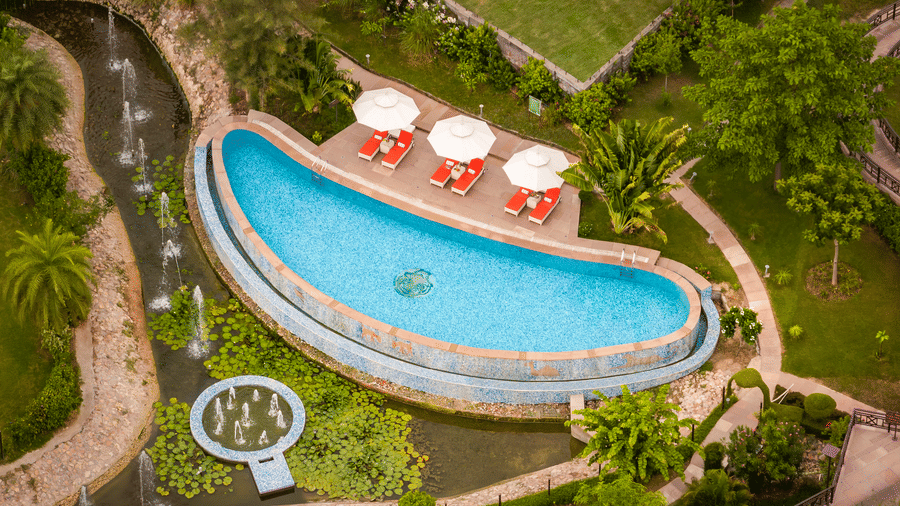 Aerial view of the outdoor swimming pool at AamaGhati Wildlife Resort surrounded by lush green garden pathways and landscaped features.
