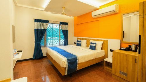 An image of a room with a bed, bed side table, a wall  mounted mirror, tea and coffee maker placed on a table, and a window overlooking the view - MGM Whispering Nest