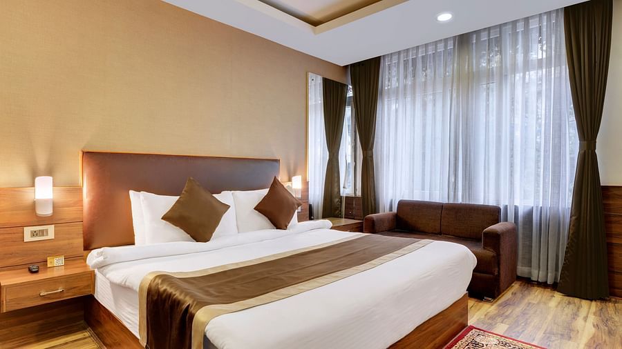 A queen bed with a sofa and side tables next to it inside Premium Room - Sumitel Shangrila, Deorali