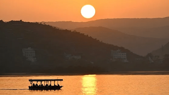 A serene sunset scene over Lake Pichola in Udaipur, with a small boat silhouetted against the horizon, a perfect way to experience the magic of Udaipur sightseeing.