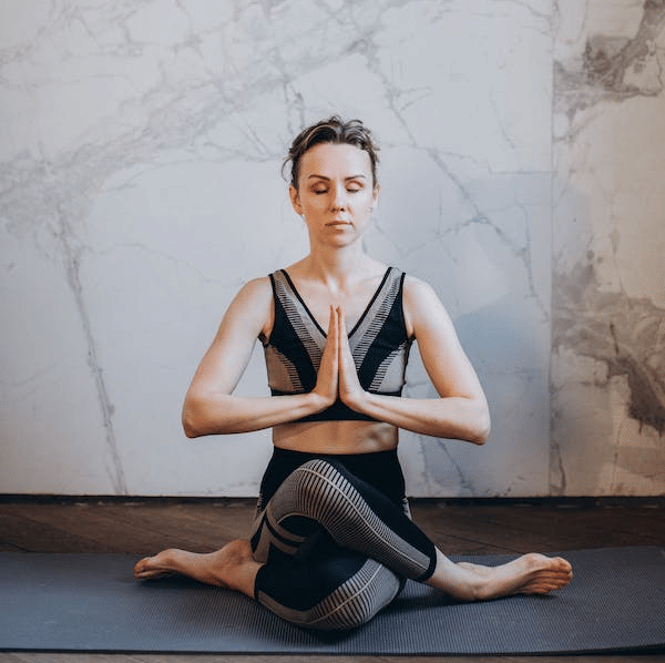 A woman with short dark hair and mesh leggings practices yoga in a seated pose with hands clasped at YO1 Longevity and Health Resorts in Catskills
