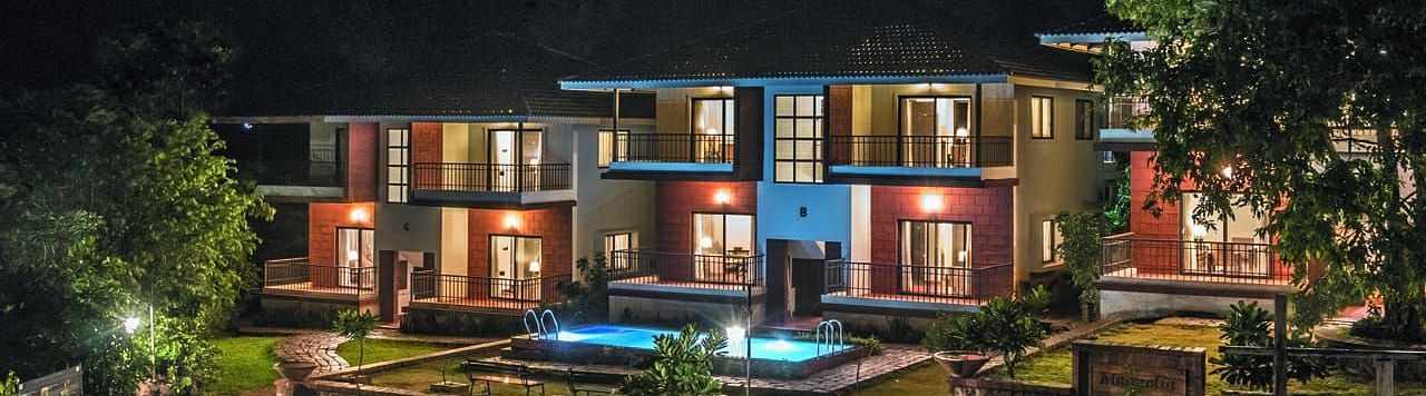 Night view of a beautifully lit resort with modern architecture, a central pool, and lush greenery.