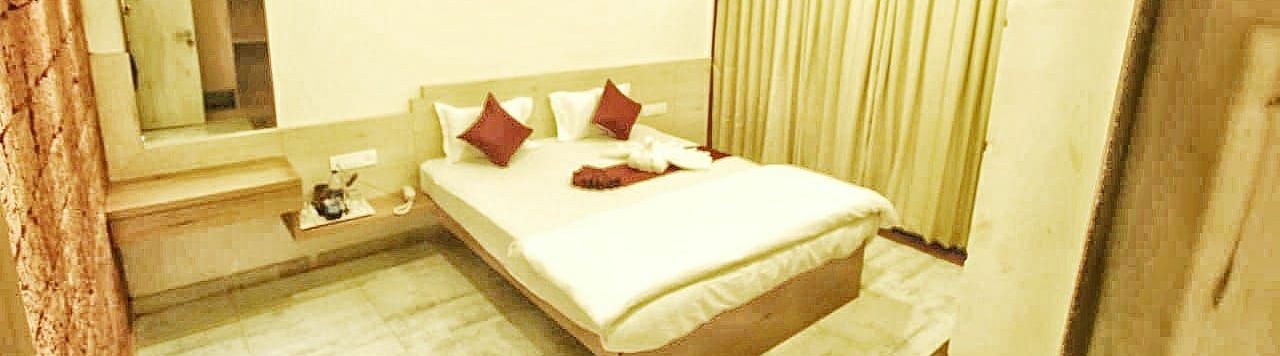 A spacious room with a large bed and windows beside it, covered with curtains. There is a wall-mounted mirror at SeaFort Beach Resort