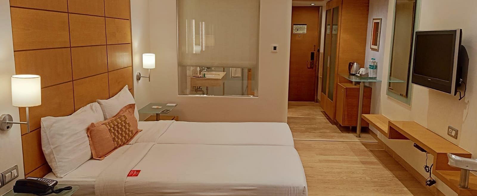 Image of twin beds in the executive twin room at our hotel featuring a flat screen television, bed side table, mirror, and other furniture. | Mirage Hotel