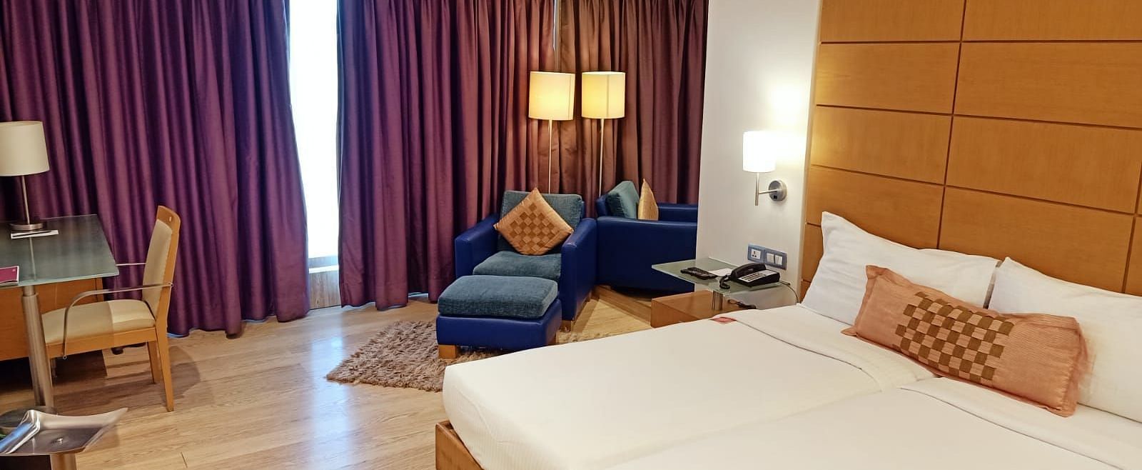 Image of twin beds in the executive twin room at our hotel featuring a flat screen television, bed side table, mirror, violet curtains, and other furniture. | Mirage Hotel