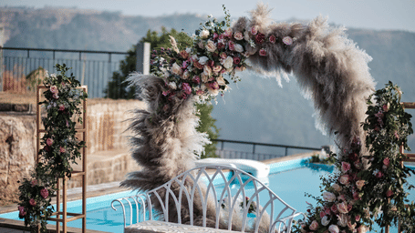 Circular floral and pampas grass wedding arch with white bench beside the infinity pool at Polo Resort Cherrapunji.