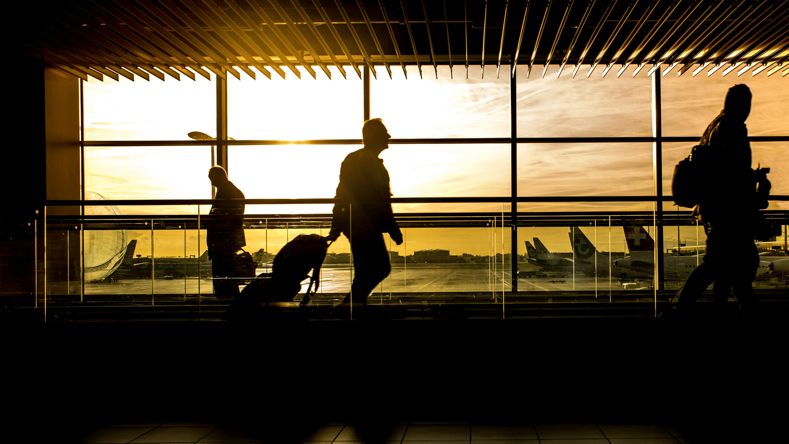 Silhouetted passengers walk through an airport terminal at sunset.