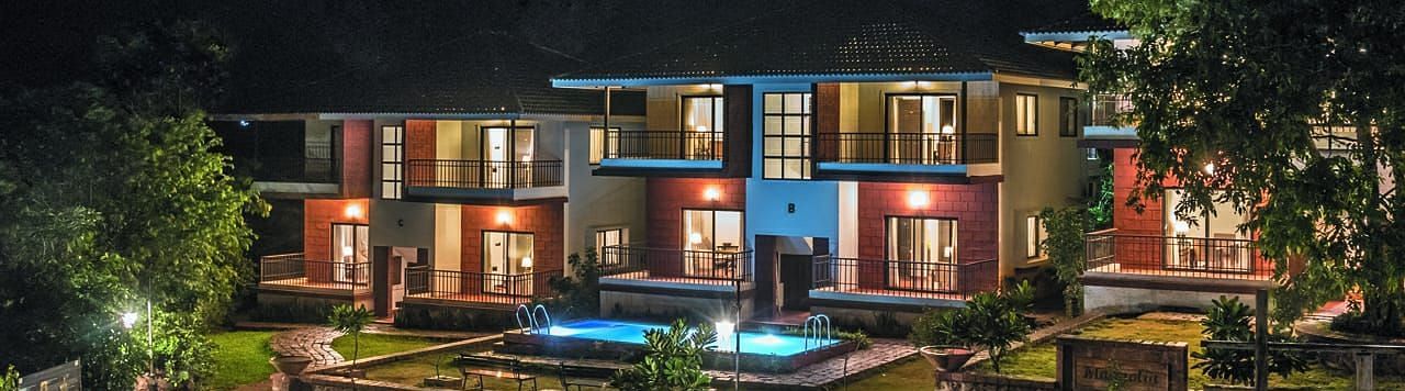 Night view of a beautifully lit resort with modern architecture, a central pool, and lush greenery.