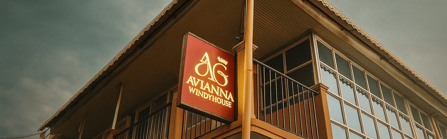 Cinematic full HD photo of Avianna Windy House exterior showing its illuminated maroon and gold signboard, warm-toned building façade, and glass-panel balcony under soft natural daylight.