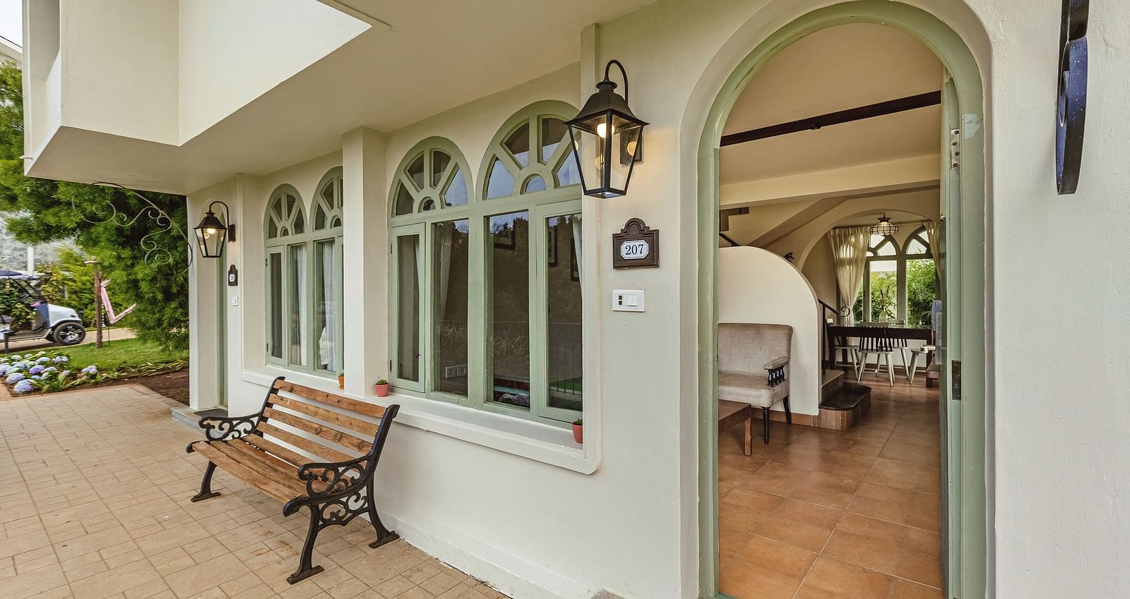 Exterior view of Mango Hill Shola, Ooty, showcasing arched windows, a structured façade, and a bench along the entrance walkway.