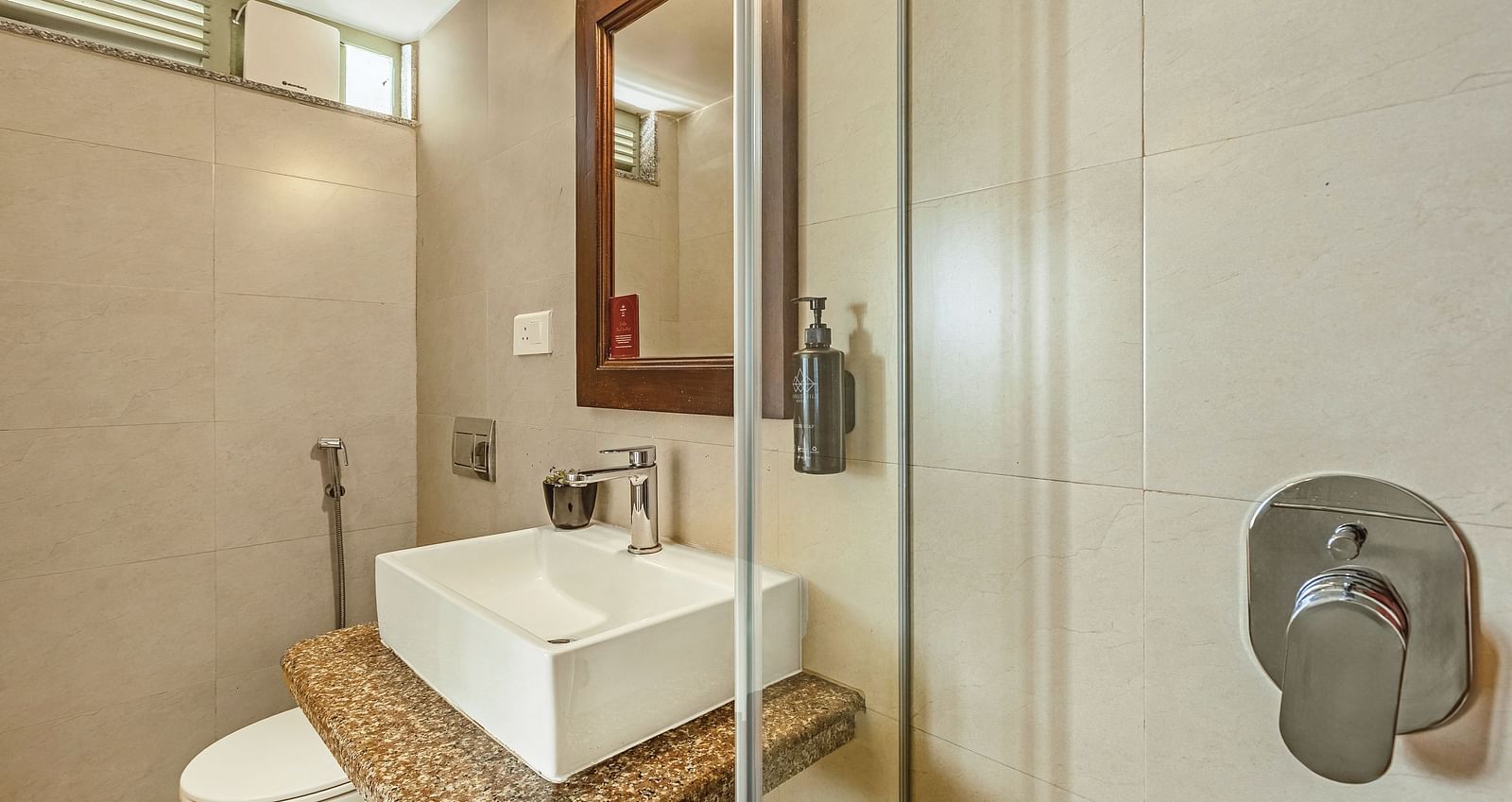 Contemporary bathroom at Mango Hill Shola, Ooty, showcasing a glass-enclosed shower, countertop basin, and a well-lit vanity mirror.