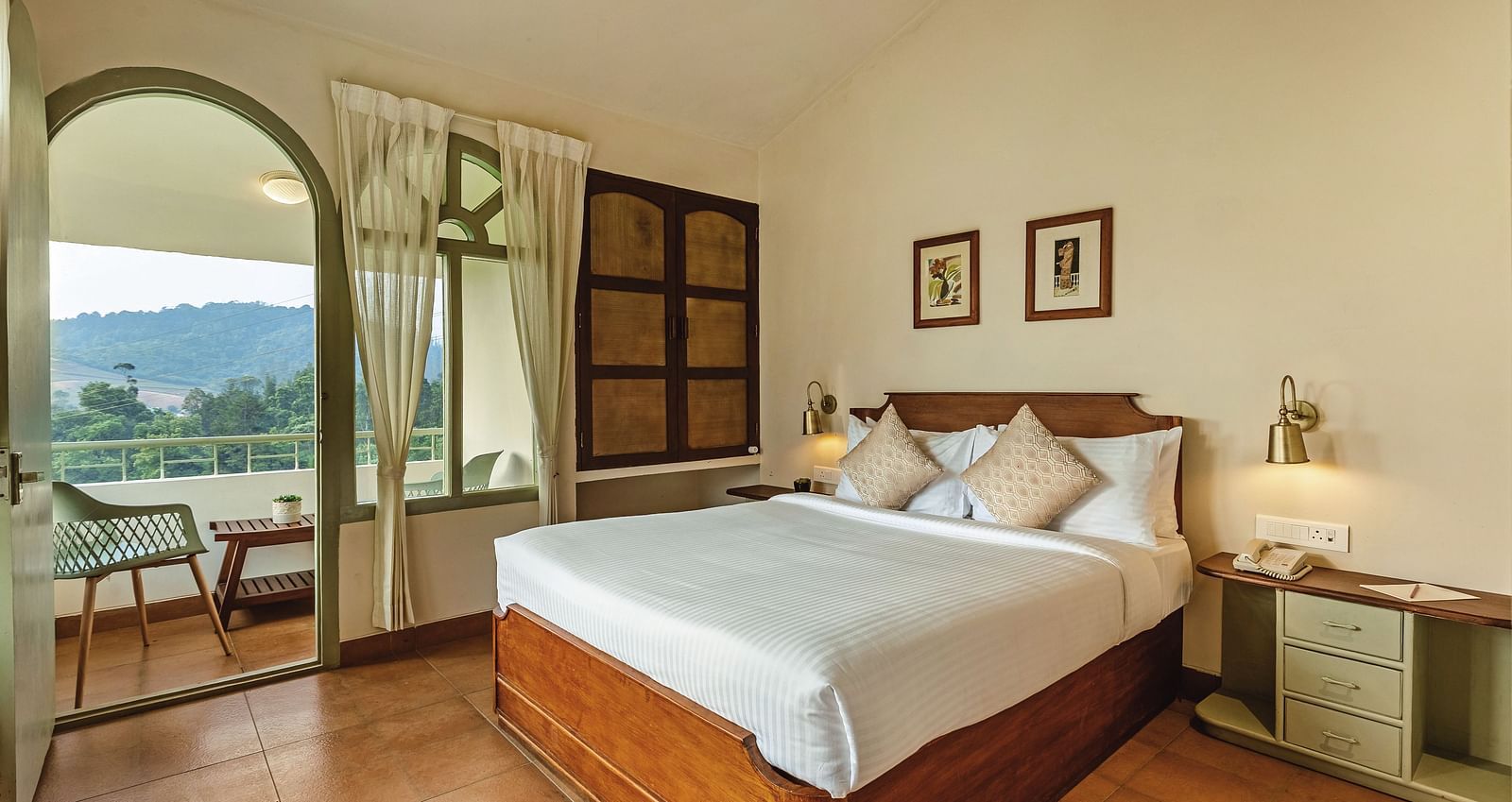 Comfortable bedroom at Mango Hill Shola, Ooty, with a plush double bed, bedside lamps, and an arched window that opens up to serene landscape views.